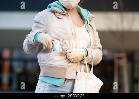 Donna in possesso di una carta di credito e indossare guanti in lattice e maschera medica monouso prima di fare acquisti di fronte a un supermercato. Protezione contro il coronav Foto Stock