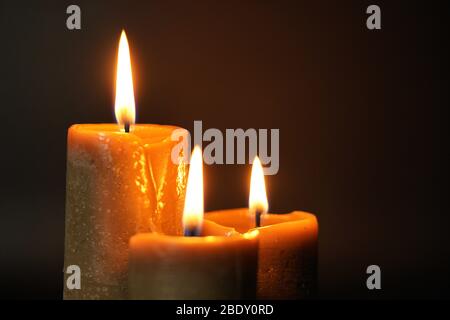 Gruppo di tre candele brune che bruciano su uno sfondo nero primo piano. Concetto di comfort, romanticismo, mistico, occultismo, religione, un simbolo di memory.Copy Foto Stock