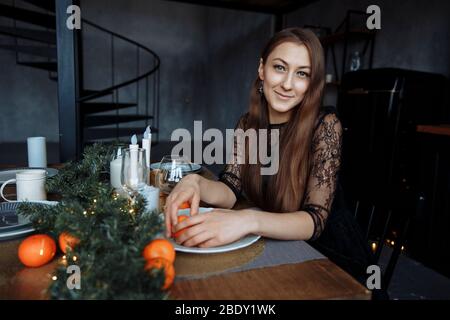 La brunetta in un abito nero pulisce un arancio in un bellissimo ambiente di Capodanno Foto Stock