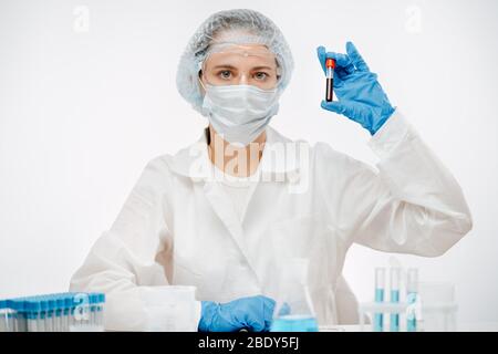 medico con maschera e occhiali di protezione che contiene il campione di sangue per l'analisi del coronavirus Foto Stock