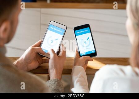 Mani di due giovani date con smartphone durante l'operazione finanziaria di invio e ricezione di denaro tramite online banking Foto Stock