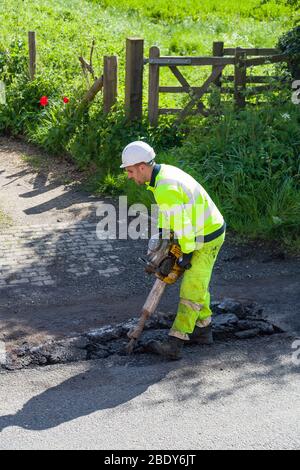 BUCKINGHAM, Regno Unito - 03 maggio 2018. Uomo che indossa indumenti ad alta visibilità per riparare buche su fondo stradale danneggiato Foto Stock