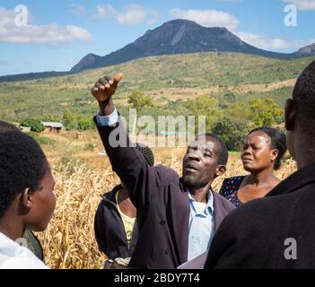 Contadino in Malawi alza la mano animatamente e parla con un gruppo di agricoltori del campo Foto Stock