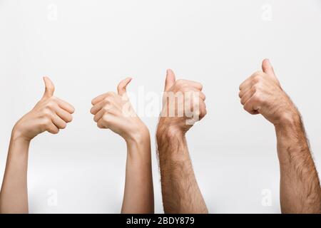 Immagine di primo piano delle mani sollevate di un uomo e di una donna isolata su sfondo bianco muro che mostra i pollici su gesto. Foto Stock