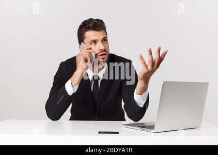 L'attraente imprenditore caucasico preoccupato e stanco parlare sul telefono cellulare seduto alla scrivania dell'ufficio che lavora in stress ha funzionato eccessivamente e frustrato. Foto Stock