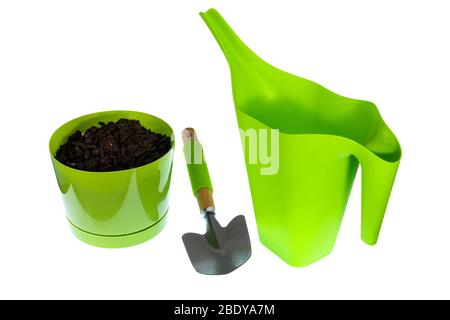 Colpo orizzontale di una lattina di irrigazione di plastica verde, una cazzuola, e una pentola di fiori di plastica verde con terreno di incapsulamento in esso. Sfondo bianco. Foto Stock