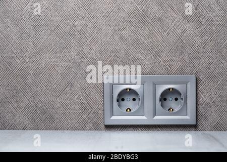 Presa grigia con messa a terra con ingresso per due dispositivi. Si trova sulla parete grigia sopra il tavolo di conteggio. Elettricità e concetto di riparazione Foto Stock