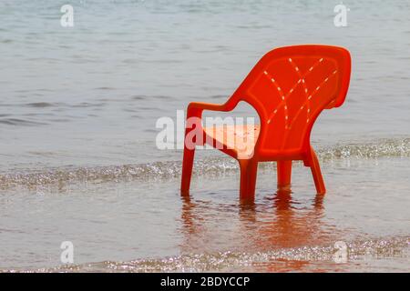 Sedia rossa in plastica in acqua vicino al mare Foto Stock