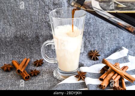 Tradizionale gegnog invernale in tazza di vetro con latte, cannella e stelle di anice ricoperte di panna montata su un panno grigio, caffè in polvere Foto Stock