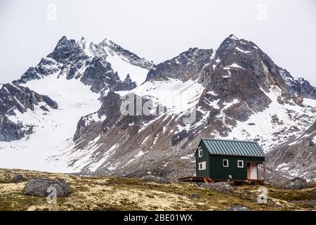 Un piccolo edificio verde nella natura selvaggia dell'Alaska offre rifugio agli sciatori e agli escursionisti del Talkeetna Mountain Range. Foto Stock