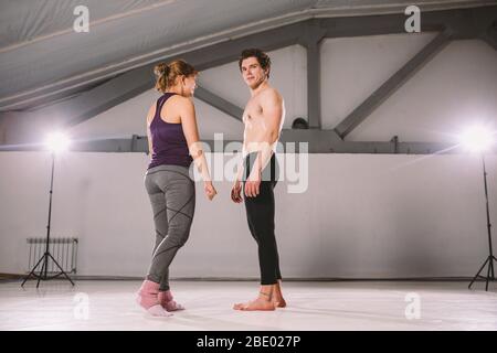 Il tema di Acroyoga e Yoga pone. Pratica di Acroyogis. Con la retroilluminazione dello studio. L'uomo base lancia il volantino donna Populs in volo. Posizione Foto Stock