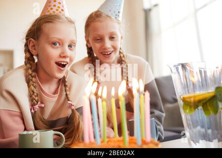 Ritratto di ragazza eccitata in cappello festa che celebra il compleanno insieme a sua sorella che mangiano torta di compleanno a casa Foto Stock