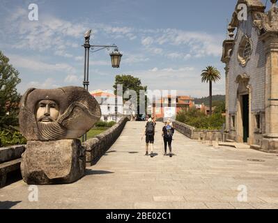 Due escursionisti femminili sul percorso centrale di Camino Portugués passeggiando davanti a una grande statua di benvenuto Bom Camino a Ponte de Lima nel Portogallo del Nord Foto Stock