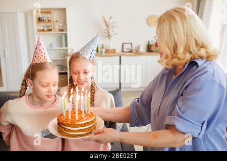 Nonna torta di compleanno di cottura con candele per le sue nipoti che celebrano il compleanno a casa Foto Stock