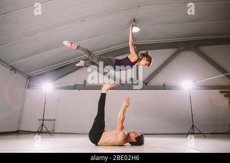 Il tema di Acroyoga e Yoga pone. Pratica di Acroyogis. Con la retroilluminazione dello studio. L'uomo base lancia il volantino donna Populs in volo. Posizione Foto Stock