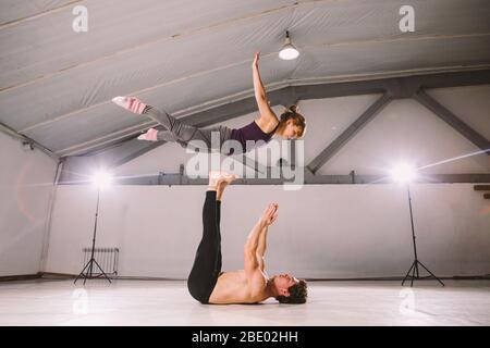 Coppia giovane che pratica acro yoga in palestra. Stile di vita sano. Acroyoga. Yoga di coppia. Yoga partner. Uomo muscolare che lancia le donne all'aria. Concetto Foto Stock