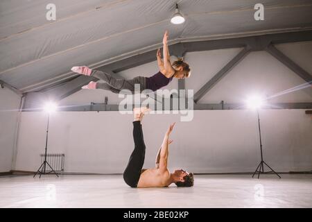Il tema di Acroyoga e Yoga pone. Pratica di Acroyogis. Con la retroilluminazione dello studio. L'uomo base lancia il volantino donna Populs in volo. Posizione Foto Stock