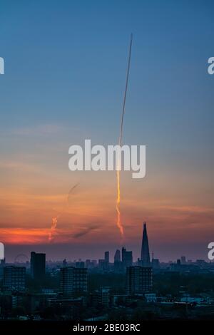 Londra, Regno Unito. 10 aprile 2020. Tempo in Gran Bretagna: Il sentiero del vapore (o controtaia) di un aereo da passeggeri è visto salire in alto sulla città al tramonto con il grattacielo Shard in vista durante l'ondata di caldo del fine settimana di Pasqua. Credit: Guy Corbishley/Alamy Live News Foto Stock