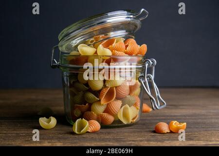 Pasta Conchiglie colorata in vaso di vetro su sfondo di legno. Vista frontale, primo piano Foto Stock