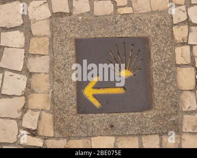 Camino de Santiago segno e freccia gialla. Simbolo di conchiglia Camino. La calotta per scallop viene utilizzata come simbolo di direzione lungo il Camino. Foto Stock