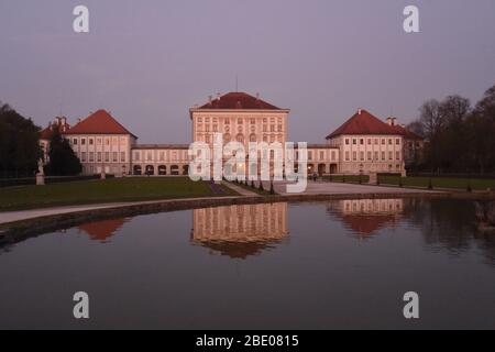 Monaco, Germania. 10 aprile 2020. Il Palazzo di Nymphenburg è illuminato di rosso dal sole serale e si riflette nell'acqua di una fontana. Quasi tutti i visitatori passano attraverso il parco a causa delle restrizioni di uscita dovute al coronavirus, che si applicano in Baviera. Credit: Felix Hörhager/dpa/Alamy Live News Foto Stock