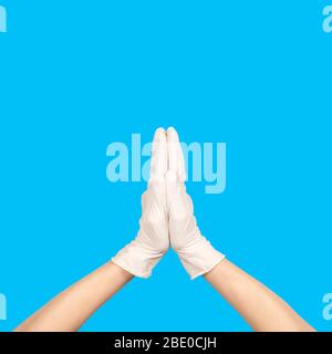 Pregate o Namaste gesto in lattice chirurgico segno guanto contro sfondo blu. Mano in un guanto in lattice bianco isolato su bianco. Gesto della mano della donna o. Foto Stock