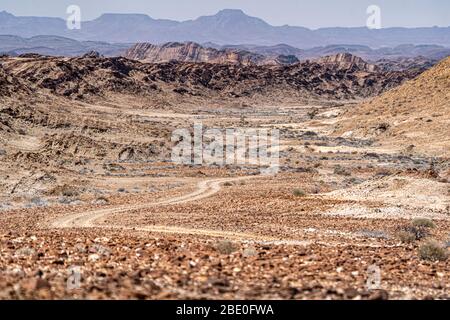Un sentiero roccioso si snoda attraverso un paesaggio lunare del deserto namibiano Foto Stock