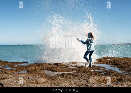 Tween startled da onda che si schiantano sopra la roccia Foto Stock