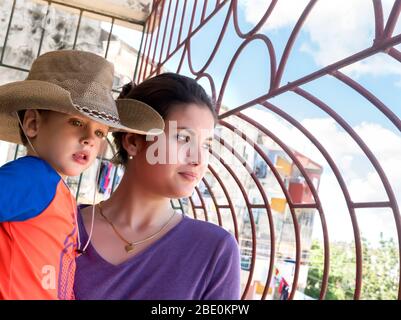 Giovane ragazza cubana che tiene un ragazzino tra le braccia guardando via attraverso le barre di ferro. Foto Stock