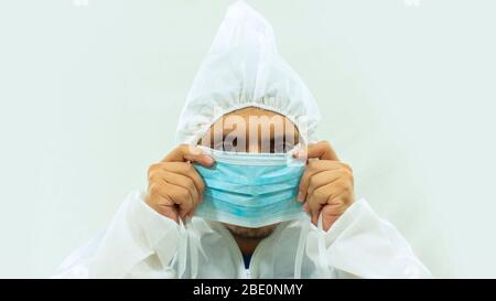 Medico in tuta bioprotettiva bianca con una maschera blu con le mani che la mette sul viso su sfondo bianco Foto Stock