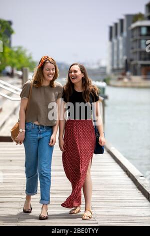 Due giovani donne che camminano lungo il porticciolo ridendo Foto Stock