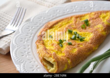 Frittata soffice con cipolle primaverili verdi e pane tostato fresco su una superficie di legno con tovagliolo e forchetta di metallo Foto Stock