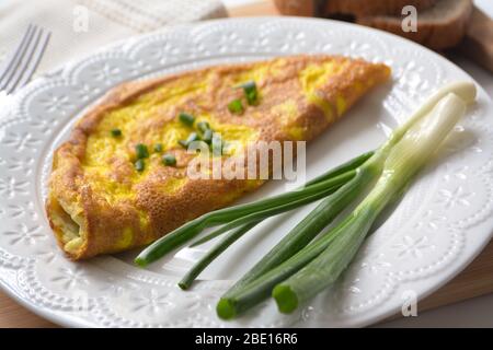 Frittata soffice con cipolle primaverili verdi e pane tostato fresco su una superficie di legno con tovagliolo e forchetta di metallo Foto Stock