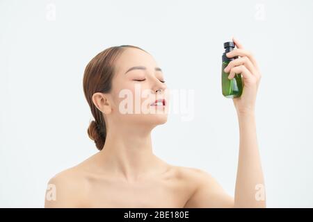 Giovane donna che applica acqua termale sul viso su sfondo bianco. Prodotto cosmetico Foto Stock