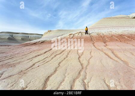 Giovane ragazzo in giacca gialla escursioni su bizzarre montagne di gesso, formazioni rocciose colorate di Boszhira in Kazakistancliff occidentale Foto Stock