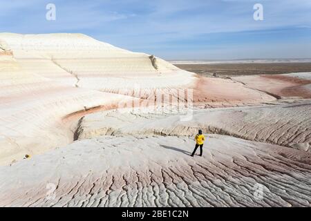 Donna in piedi a bizzarre montagne di gesso, colorate formazioni rocciose di Boszhira in Kazakistancliff occidentale Foto Stock