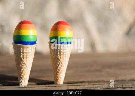 Famiglia di coppie LGBT. Uova con bandiera lgbt colore in gelato waffle cono su natura primavera sfondo esterno. Idea creativa per illustrazione parata gay, festa lgbt, matrimonio omosessuale, giorno dei valentines. Foto Stock