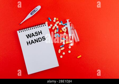 Notepad, una varietà di medicinali, termometro, siringa e fiale con medicinale su sfondo rosso. Sul blocco note è la scritta Wash Hands Foto Stock