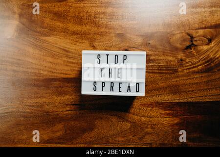 Testo "Stop the spread" in una casella luminosa su sfondo di legno. Foto Stock