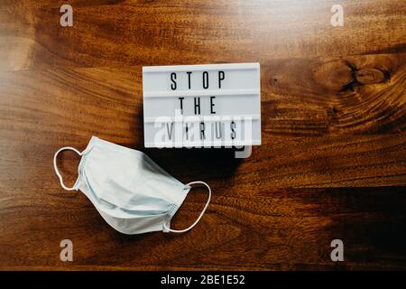 Testo "Stop the virus" in una scatola luminosa con maschera medica su sfondo in legno. Foto Stock