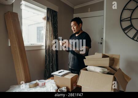 Un uomo con tatuaggio come il venditore prepara la scatola di consegna per il cliente, vendite in linea, o ecommerce. Concetti di shopping online. Controllo di un ordine. Foto Stock