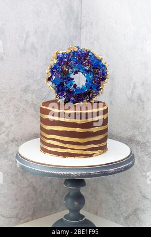 Torta moderna al cioccolato con strisce dorate e geode isomalt blu. Sfondo grigio. Foto Stock