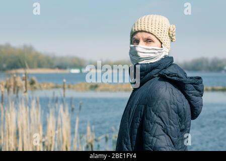 Una povera donna anziana indossa una maschera casalinga per proteggersi da virus come il coronavirus, noto anche come covid-19, o SARS e MERS. Si siede sopra Foto Stock