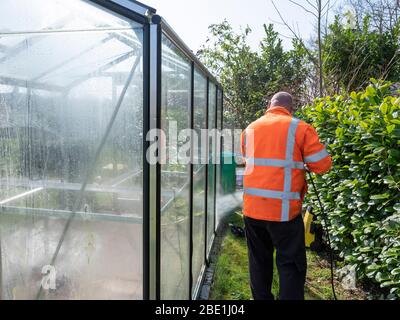 Addetto alle costruzioni che pulisce la sporcizia con pulitore ad alta pressione da una serra di vetro. Foto Stock