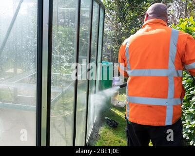 Addetto alle costruzioni che pulisce la sporcizia con pulitore ad alta pressione da una serra di vetro. Foto Stock