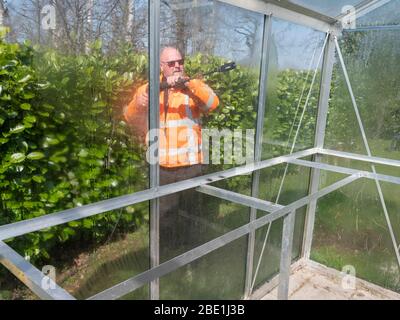 Addetto alle costruzioni che pulisce la sporcizia con pulitore ad alta pressione da una serra di vetro. Foto Stock