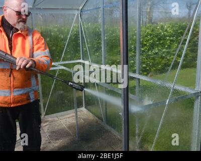 Addetto alle costruzioni che pulisce la sporcizia con pulitore ad alta pressione da una serra di vetro. Foto Stock