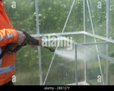 Addetto alle costruzioni che pulisce la sporcizia con pulitore ad alta pressione da una serra di vetro. Foto Stock