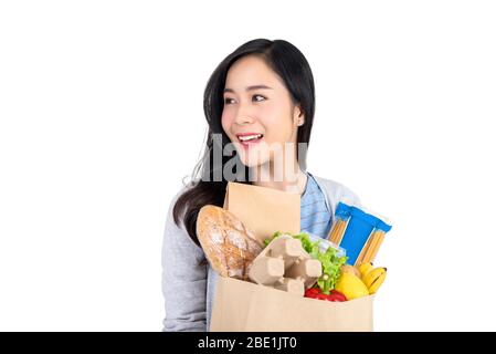 Bella donna asiatica sorridente che tiene la borsa della spesa della drogheria e che guarda via allo spazio vuoto da parte isolato su sfondo bianco Foto Stock