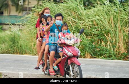 Una famiglia tailandese che viaggia su una moto, tutte indossando maschere facciali protettive, prese a Pathumthani, Thailandia, nel mese di aprile 2020. Foto Stock